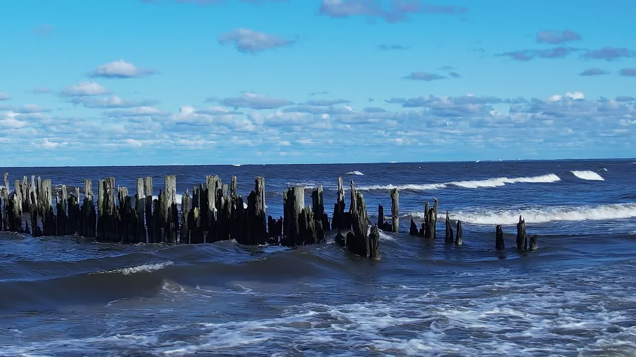 Le onde si infrangono contro vecchie strutture in legno nel Mar Baltico sotto un cielo azzurro