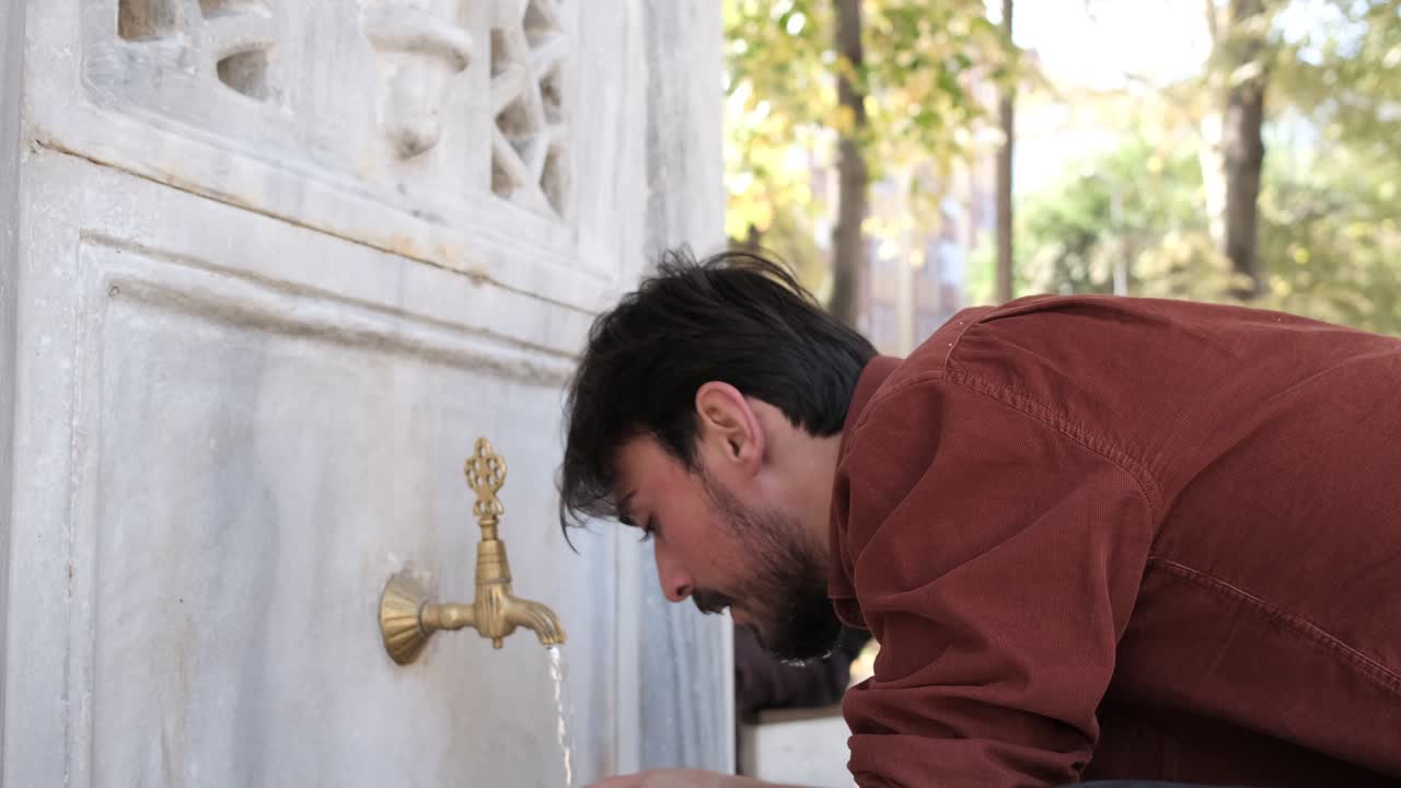 Side view of a Muslim bearded man performing ablution, a man washing his face in a mosque fountain, man turning off the fountain