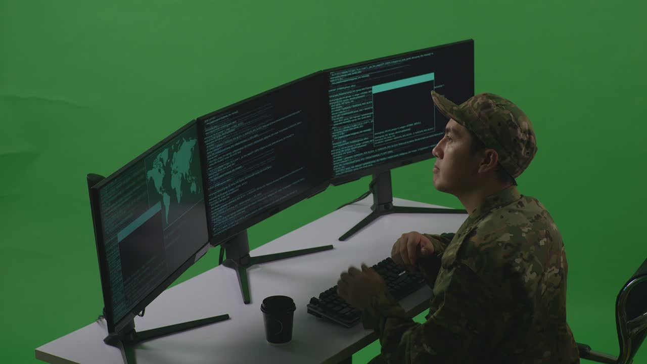Side View Of Asian Man Soldier Developer Thinking About Something Then Raising His Index Finger While Write Code With Multiple Computer Screens In Green Screen Studio