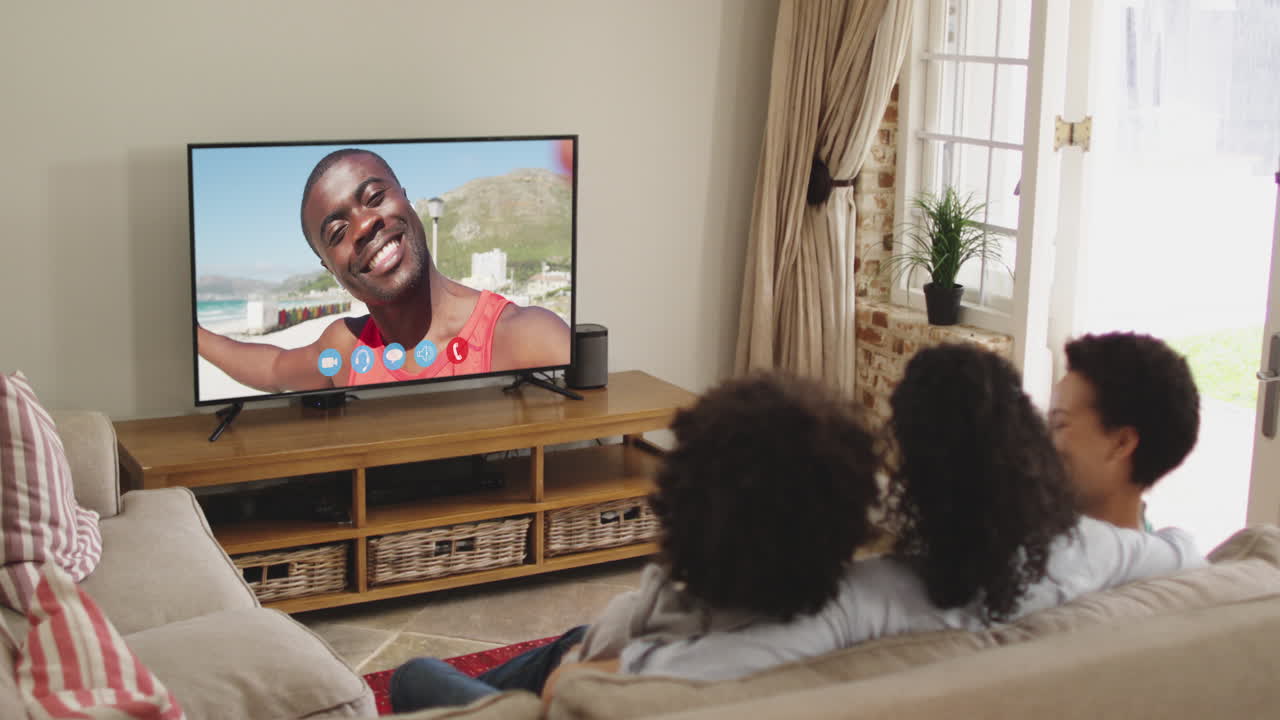 Famiglia afroamericana seduta sul divano che fa una videochiamata con un amico sullo schermo della TV.