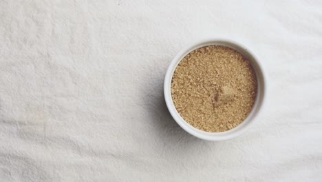 Raw-brown-sugar-in-white-ceramic-tableware-on-white-mat