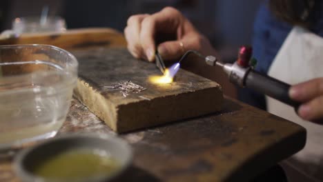 close up of hands of caucasian female jeweller using gas burner, making jewelry