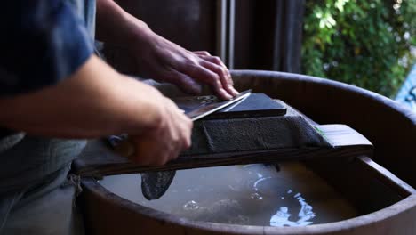 person meticulously sharpening a knife on a wet stone