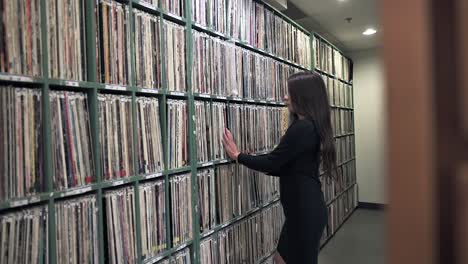 Mujer-Joven-Volviendo-A-Poner-El-Disco-Fonográfico-En-El-Estante-De-La-Biblioteca-De-Música