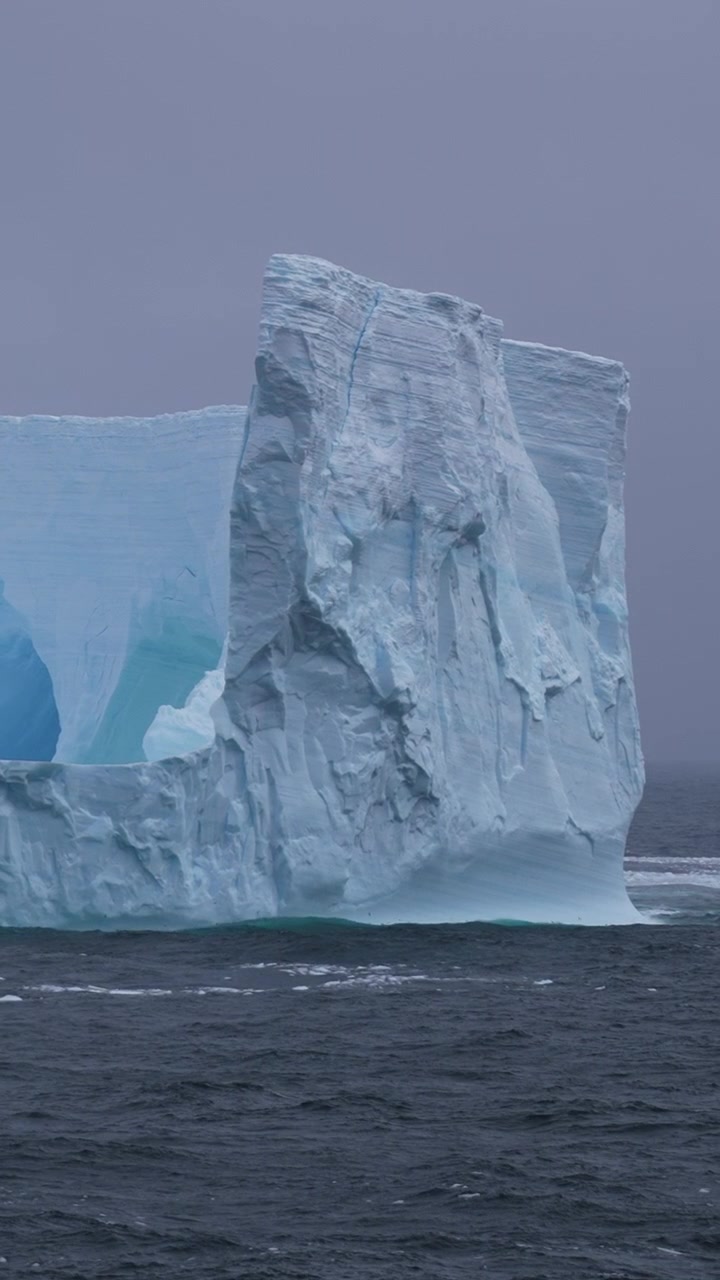 Vertical View of Massive Iceberg in Cold Arctic Ocean Water on Misty Day, Slow Motion