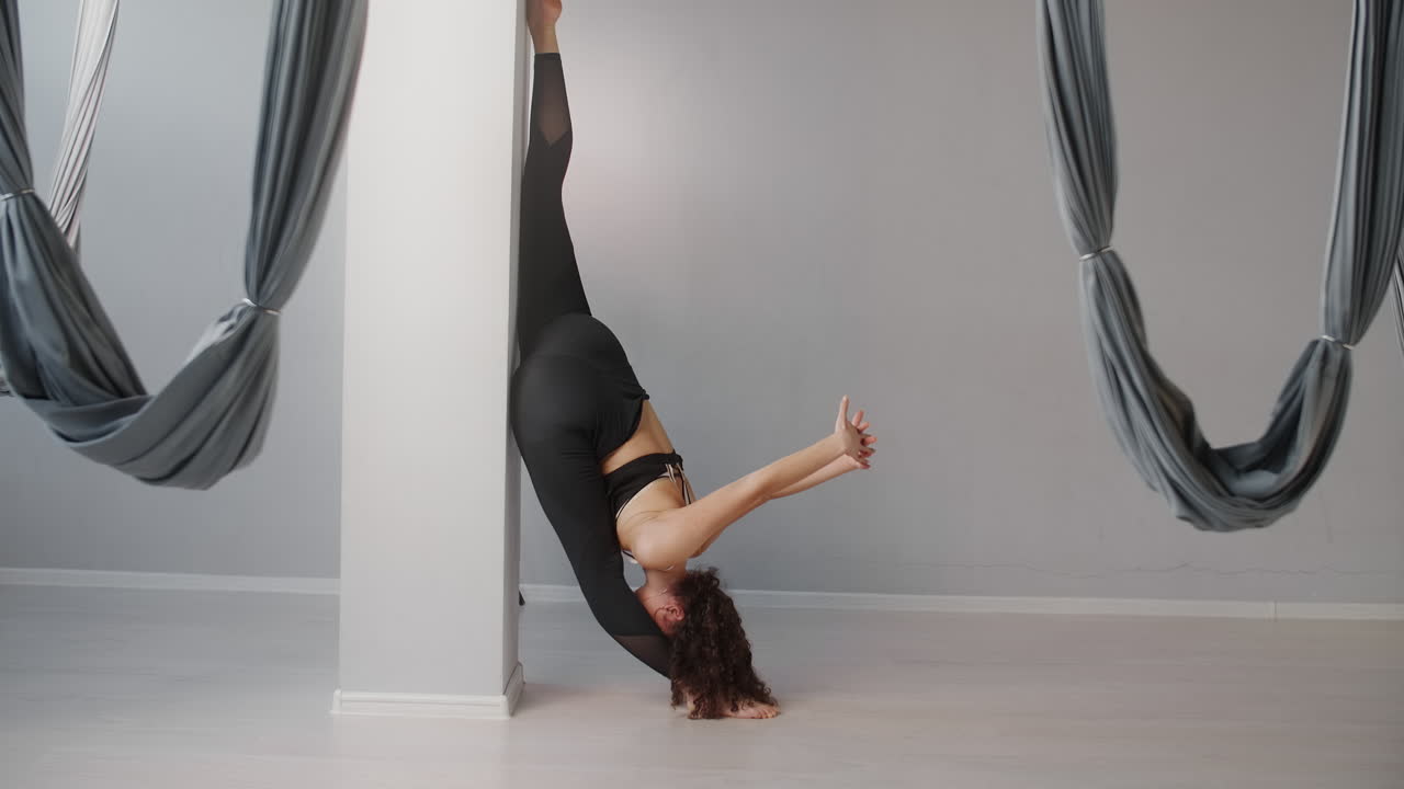 Woman practicing aerial yoga and stretching near a pillar