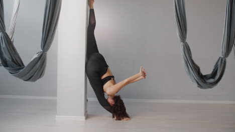 woman practicing aerial yoga and stretching near a pillar