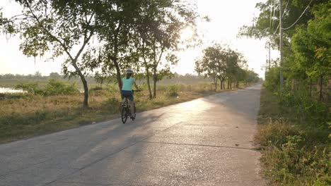 A-stationary-panning-footage-of-a-female-cyclist-riding-her-bike-along-an-empty-street-in-Isan,-Thailand