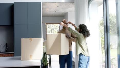 Happy-biracial-couple-talking-and-carrying-cartons-at-new-house,-slow-motion