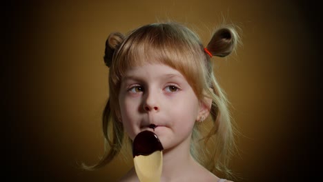 niña feliz lamendo chocolate derretido, niño comiendo, disfrutando de comida dulce no saludable en el interior