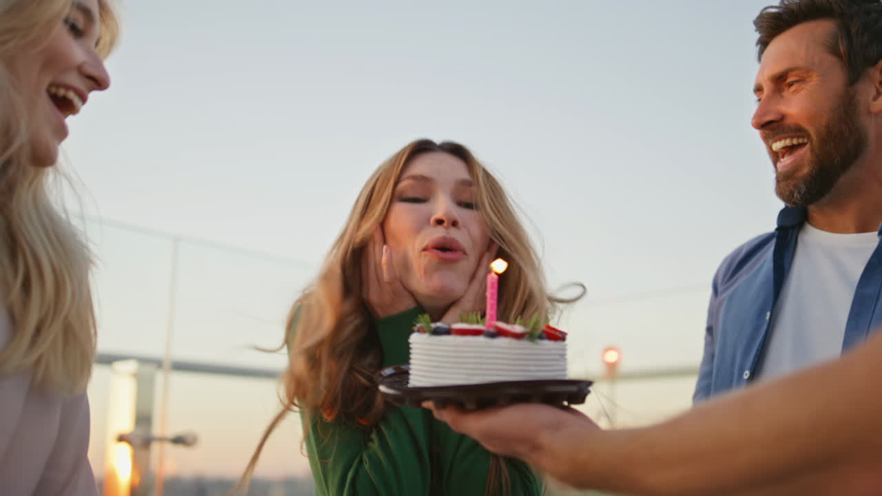 amigos llevando pastel de cumpleaños a una mujer sonriente en una fiesta en la azotea de cerca.