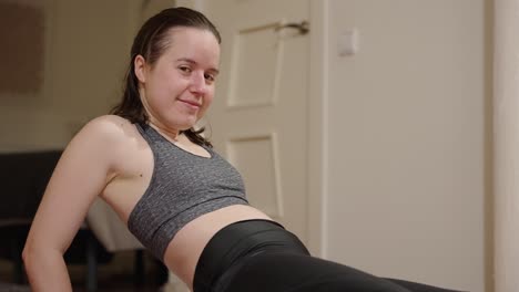 entrenamiento en casa, mujer joven mirando a la cámara mientras mantiene posiciones de estrés