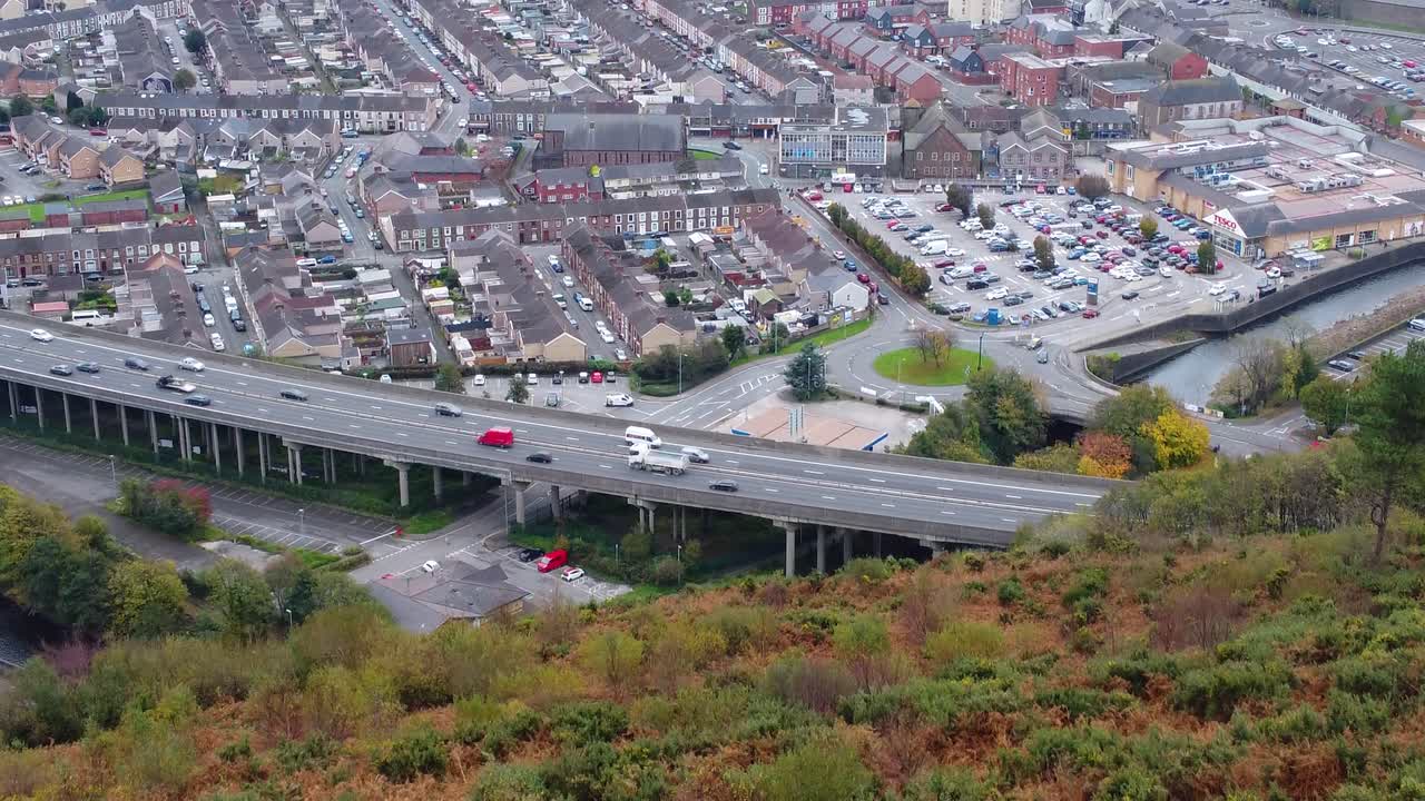 Luchtopname boven Port Talbot met gestaag verkeer op een dubbele rijbaan met auto's, vrachtwagens, bestelwagens en een grote parkeerplaats op de achtergrond 4K