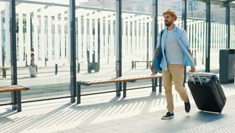 caucasian traveller wearing hat with backpack and carrying suitcase in the bus stop