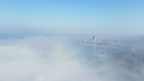 Niebla-En-Los-Emiratos-árabes-Unidos:-Vista-Aérea-De-La-Niebla-Sobre-El-Lago-Khalid-De-Sharjah,-El-Horizonte-De-Sharjah-Y-La-Isla-De-La-Bandera-Cubierta-Por-La-Niebla-De-La-Mañana-De-Invierno,-Emiratos-árabes-Unidos,-Imágenes-De-Drones-De-4k