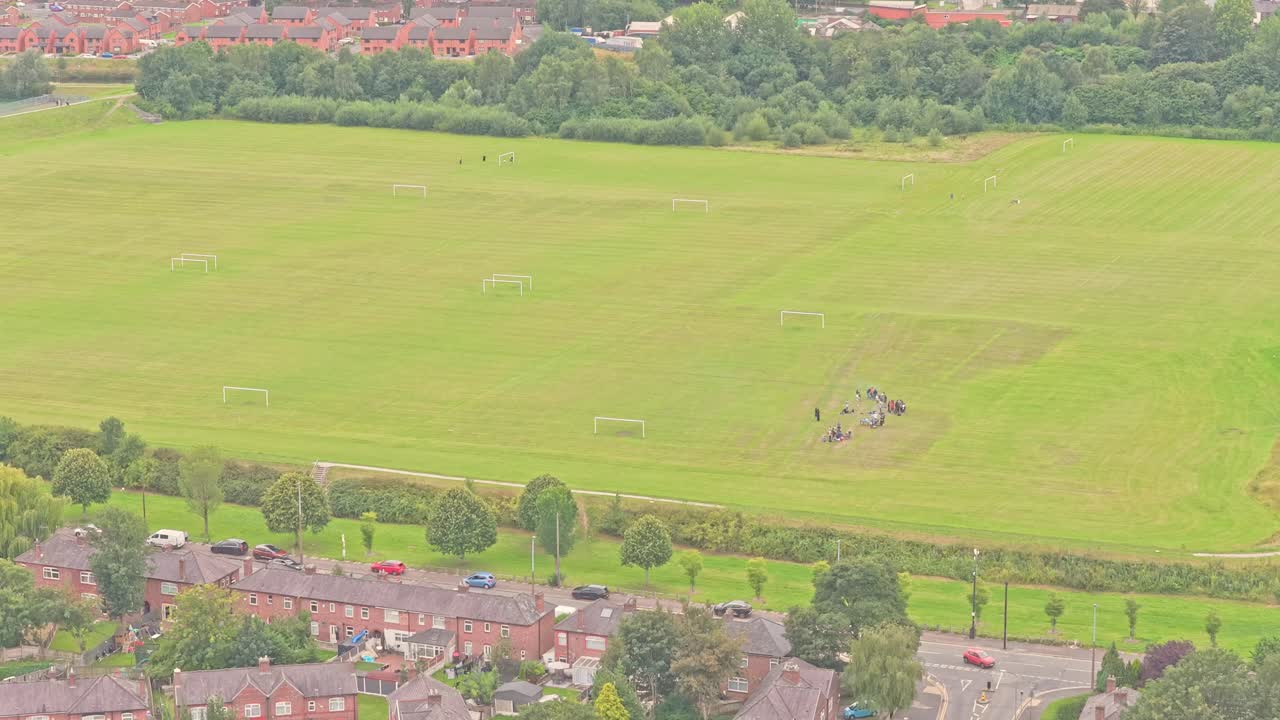 Expansive grass football pitches with multiple goalposts border brick residential streets in Salford, England, captured in high-angle aerial view