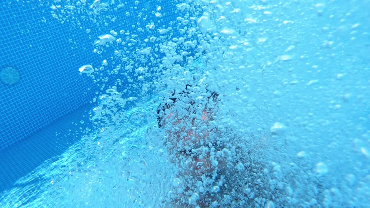 Man jumping into the swimming pool. Healthy man holding underwater camera and jumping into blue water of the pool. Summer vacation.