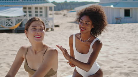 chicas aplicando protector solar en una playa de arena. una pareja lgbt feliz tomando el sol