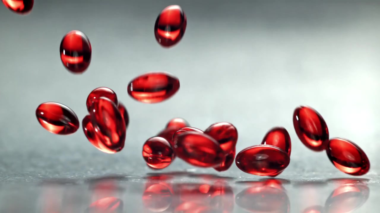 Capsule traslucide rosse che cadono al rallentatore su superficie riflettente