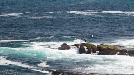 Rock fisherman on a rock outcrop with waves crashing onto rocks at Maroubra Beach, Australia