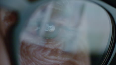 pantalla de ojo macro de cerca que se refleja en las gafas anciana navegando en línea por la noche