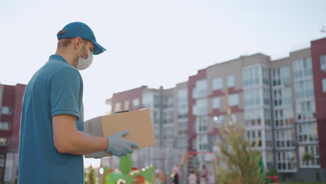 an young mailman courier with a protective mask and gloves is delivering a parcel directly to a customer home with safety. concept of courier home delivery e-commerce shipping virus covid