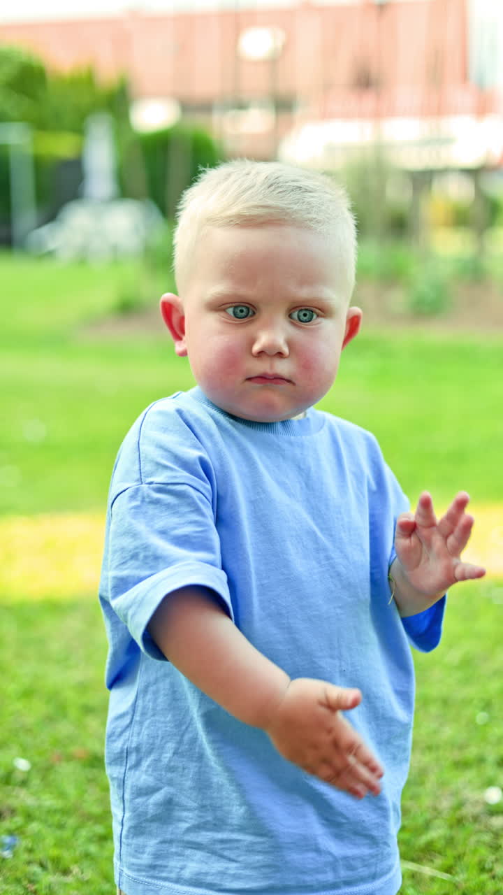 Süßer Junge in blauem T-Shirt und blauen Shorts bei einem Spaziergang im Park. Das Kleinkind geht einen Pfad entlang, inmitten von hohem Gras. Vertikales Video.
