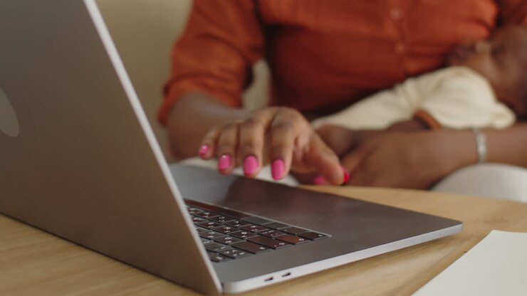 Femme discutant en visioconférence avec des collègues sur un ordinateur portable tout en tenant sa fille nouveau-née