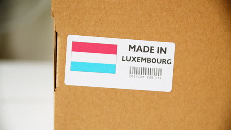 hands applying made in luxembourg flag label on a shipping cardboard box with products