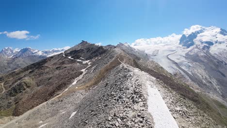 Flight-over-a-long-hiking-trail-ridge-at-Alps-mountains-in-Gornergrat,-Zermatt,-in-Switzerland,-Europe