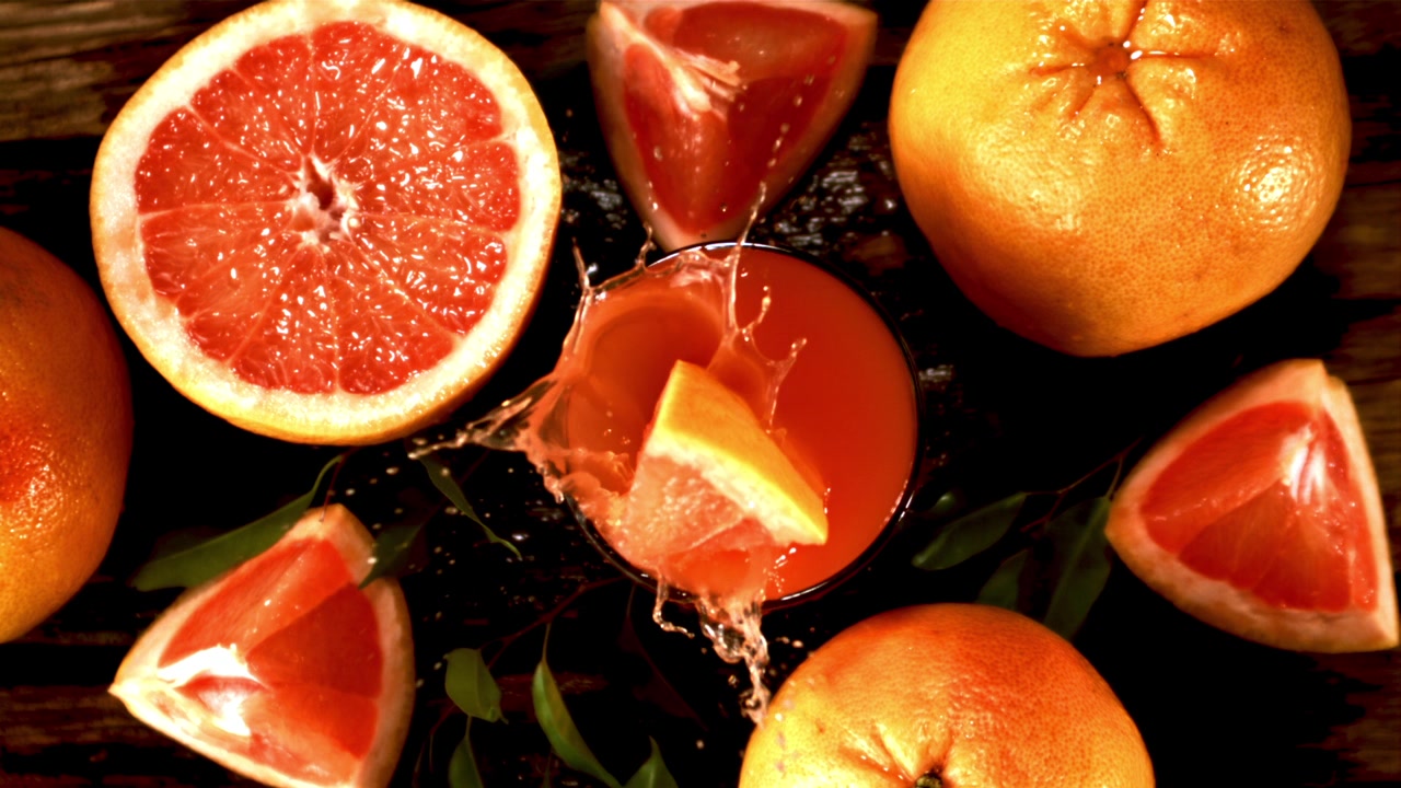 Spicchio di pompelmo che schizza nel succo al rallentatore con pompelmi freschi