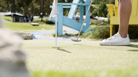 Man-with-hairy-legs-putts-ball-into-hole-at-golf-course