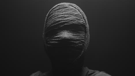 a mummy of a woman on a dark backdrop slowly rises her head