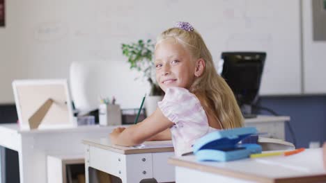 Video-of-happy-caucasian-girl-sitting-at-desk-in-classroom