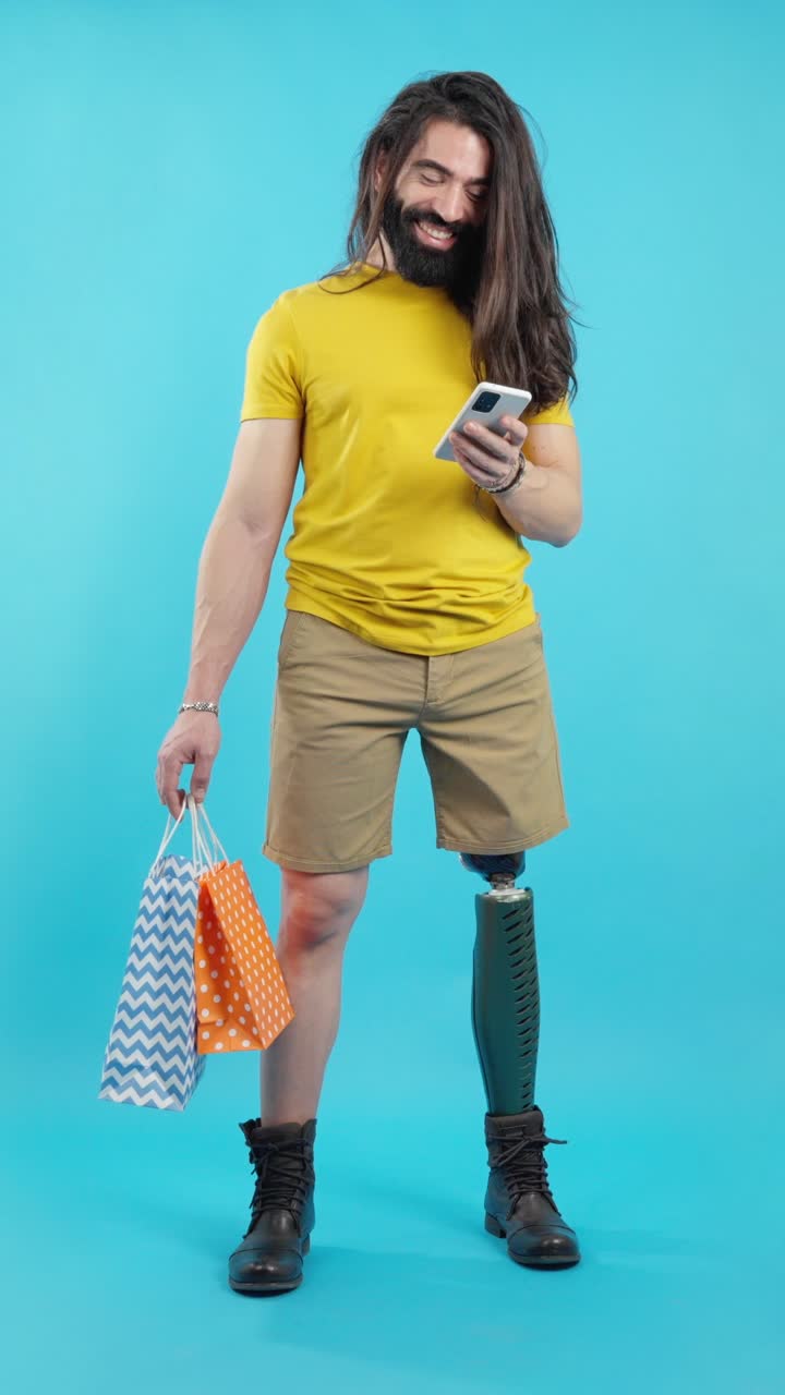 Smiling man with prosthetic leg using smartphone and holding shopping bags