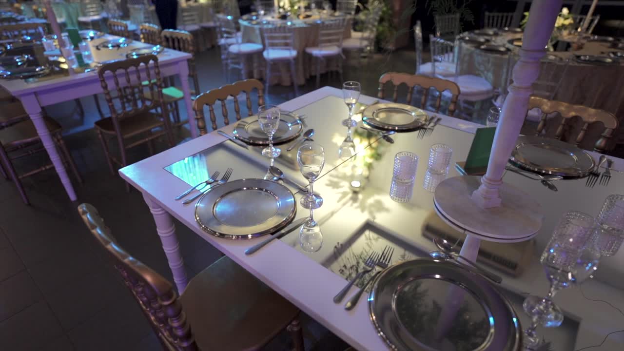 Mirrored banquet table set for four features silver charger plates, crystal glasses, and ornate gold chairs, captured in a graceful orbiting shot that highlights luxury and formal event ambiance