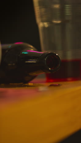 video vertical de primer plano de vino vacío y botella goteando en la mesa después de la fiesta de la casa 1