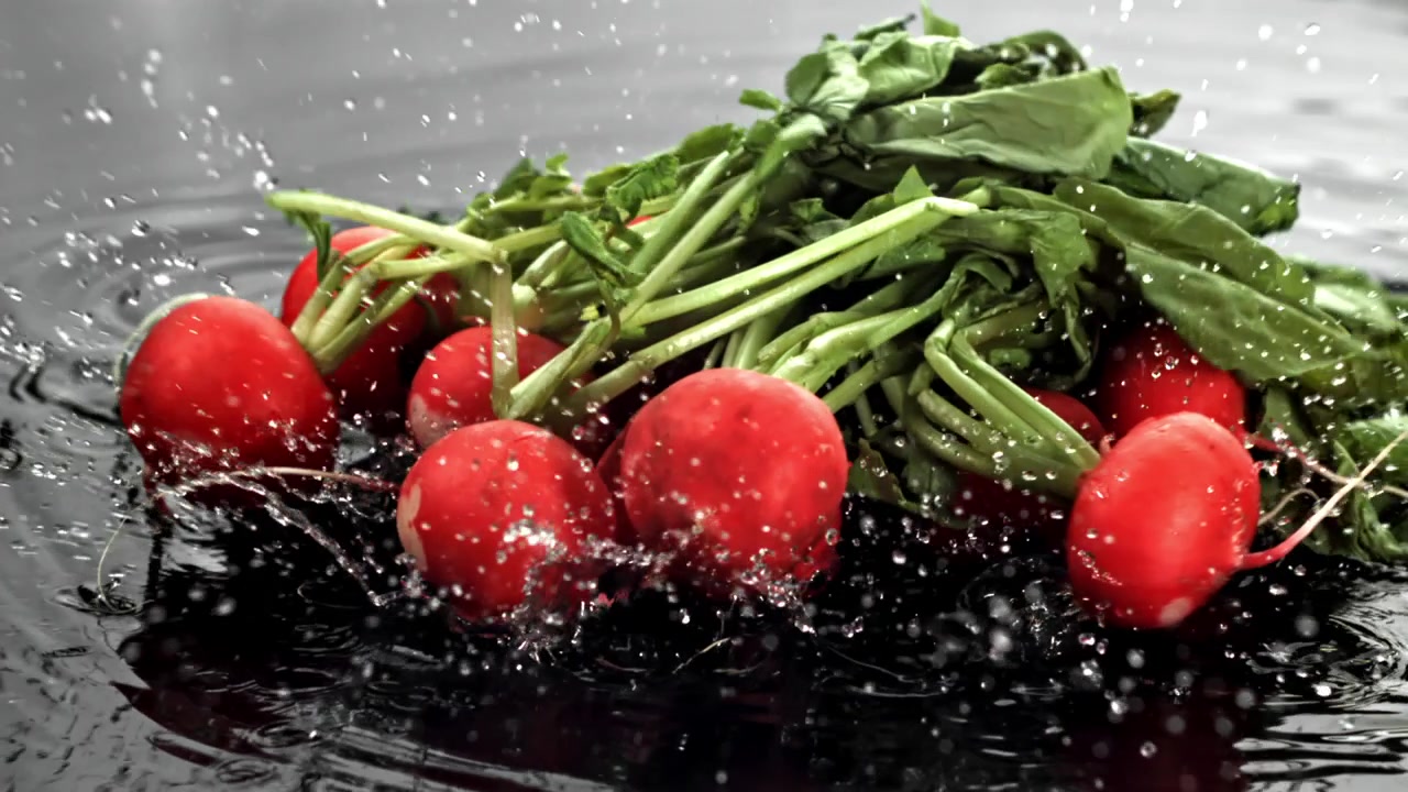 Fresh Radishes with Green Leaves Splashing into Water in Slow Motion