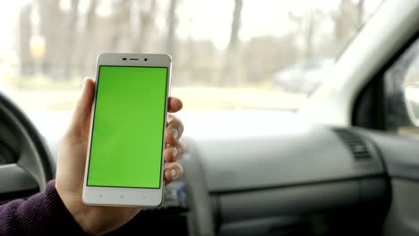 una mano sosteniendo un teléfono inteligente con pantalla verde en blanco en el coche para la dirección, masaje, ubicación, negocio. hombre se sienta en un coche moderno y trabaja en teléfono inteligente - pantalla verde - primer plano. llave de croma.