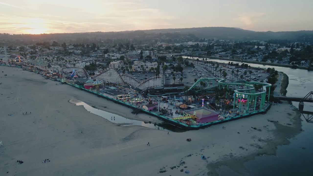 A blue hour slow motion panning drone shot of the Santa Cruz Beach Boardwalk with people riding rides and enjoying the nightlife of a carnival atmosphere on the Pacific Ocean Beach
