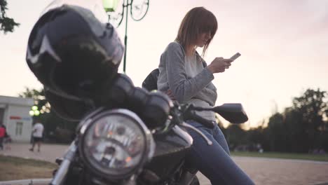 attractive young red-haired woman uses smatphone in park at sunset