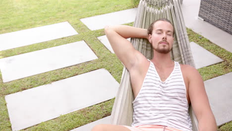 a young caucasian male relaxes in a hammock in the backyard at home, eyes closed, copy space