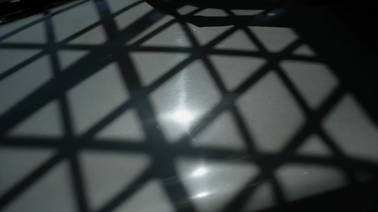 Shifting light moving bright highlight across glossy table indoors with grid shadow, dark corner