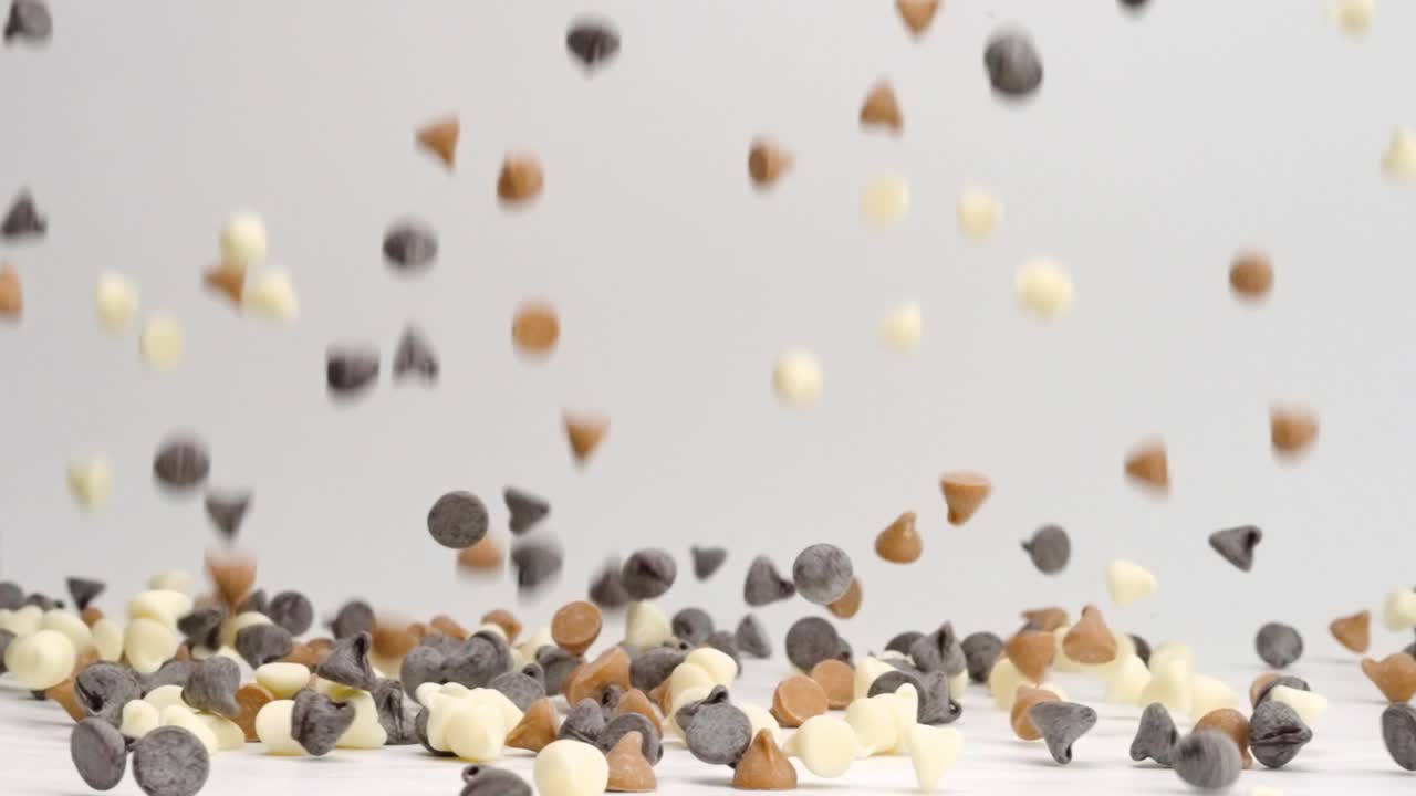 우유 세미 스위트, 버터스카치 캐러멜, 화이트 초콜릿 칩이 흰색 테이블 위에 슬로우 모션으로 떨어지고 튀는