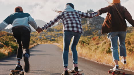 jóvenes amigos multiétnicos longboarding juntos tomados de la mano montando en patineta navegando cuesta abajo en la carretera del campo divirtiéndose disfrutando de unas vacaciones de verano relajadas