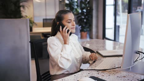 Fröhliche-Frau,-Die-Im-Büro-Auf-Dem-Smartphone-Spricht