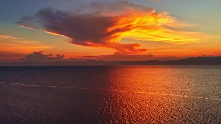 Bellissimo tramonto arancione sul mare calmo con nuvole vivaci che si riflettono sulla superficie dell'acqua