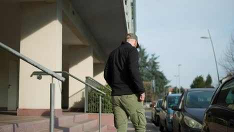 male wearing baseball cap placing magsafe wireless charging battery pack on back of iphone outside, placing in pocket and walking off down street past parked cars