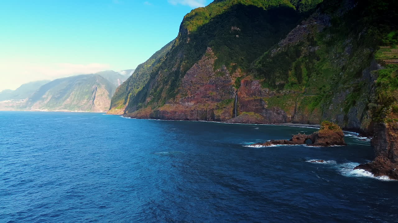 Huge mountains covered with green moss at the coastline of the Madeira Islands, Portugal. Flight over the waterscape of the Atlantic Ocean with a low angle view at the rocks.