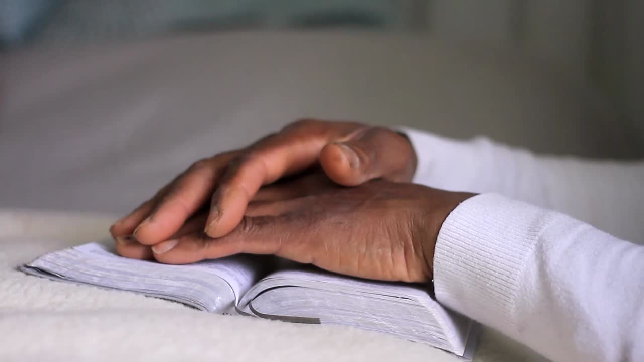 Filmato d'archivio: uomo caraibico che prega Dio con le mani giunte e una Bibbia, su sfondo bianco.